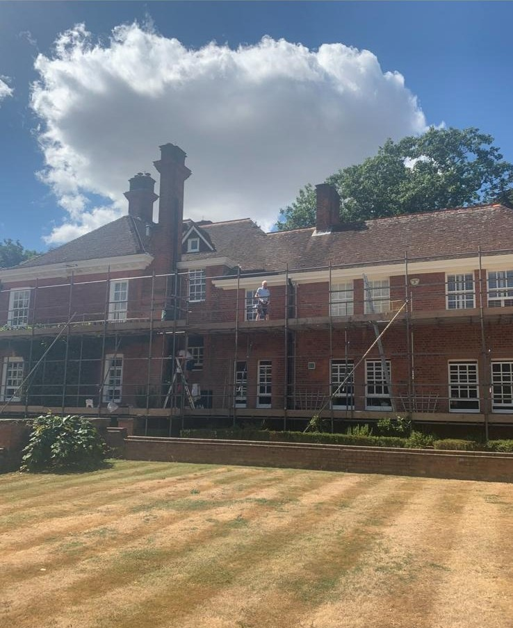 Aaron Neill on scaffolding mid-project, painting the exterior of a red-brick country house